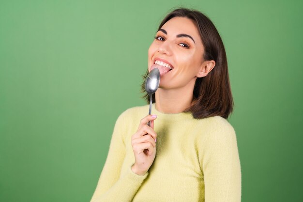 Junge Frau auf Grün in einem gelben Pullover mit Appetit isst von einem Esslöffel und genießt