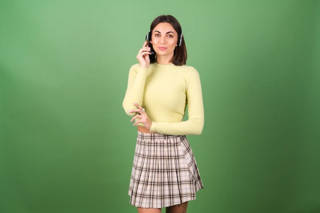 Junge Frau auf Grün in einem gelben Pullover und einem karierten Rock, Manager, Supportmitarbeiter, Verkäufer, die Anrufe von Kunden gerne entgegennimmt