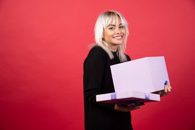 Junge Frau aufgeregt über ein Geschenk auf einem roten Hintergrund