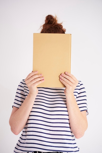 Junge Frau bedeckt ihr Gesicht mit Buchschuss