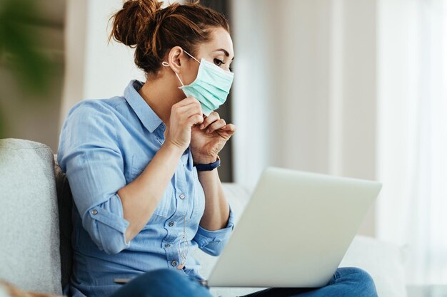 Junge Frau benutzt Laptop und lernt online, wie man Gesichtsmaske während der Virusepidemie richtig trägt