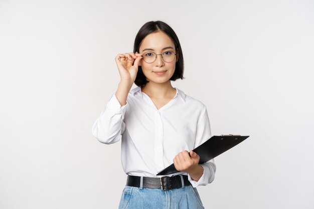 Junge Frau Büroangestellter Manager in Gläsern hält Klemmbrett und sieht aus wie eine professionelle Stellung vor weißem Hintergrund