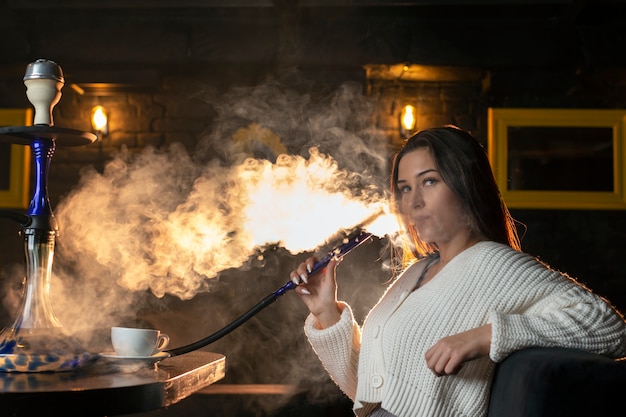 Kostenloses Foto junge frau dampft von einer wasserpfeife in einer bar