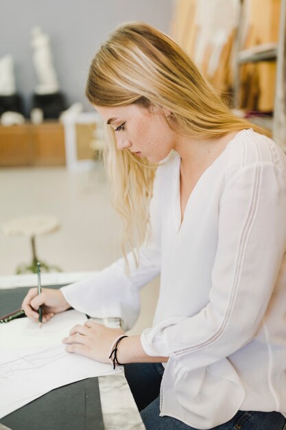 Junge Frau der Seite, die auf Papier mit Bleistift auf dem Werktisch skizziert