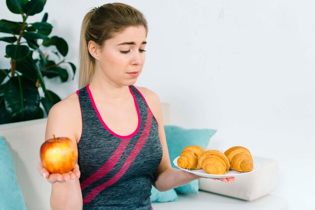 Junge Frau der verwirrten Eignung, die Apfel und Hörnchen in beiden Händen hält