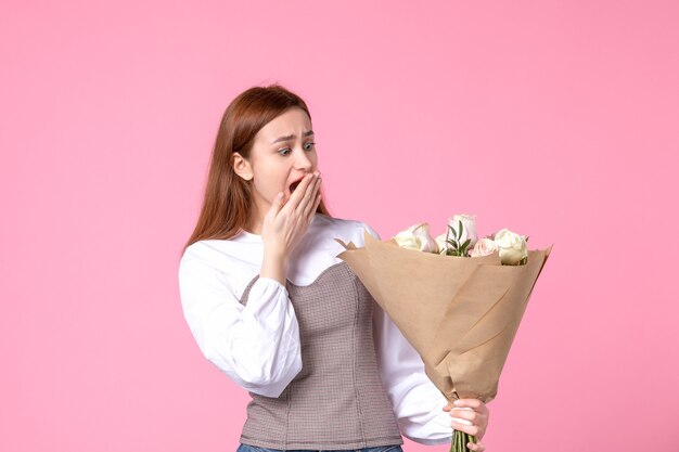 Junge Frau der Vorderansicht, die Blumenstrauß von schönen Rosen auf Rosa hält