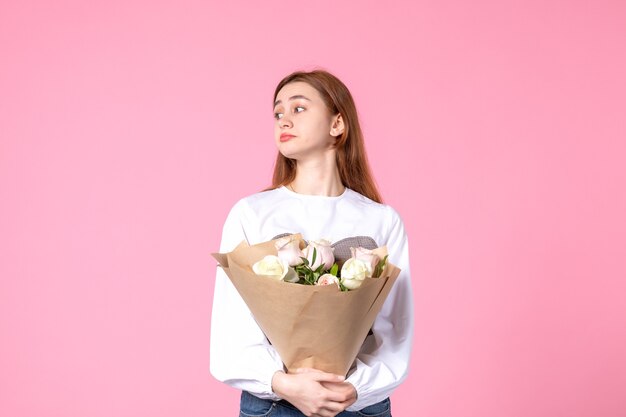 Junge Frau der Vorderansicht, die Blumenstrauß von schönen Rosen auf Rosa hält