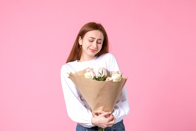 Junge Frau der Vorderansicht, die Blumenstrauß von schönen Rosen auf Rosa hält