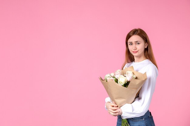 Junge Frau der Vorderansicht, die Blumenstrauß von schönen Rosen auf Rosa hält