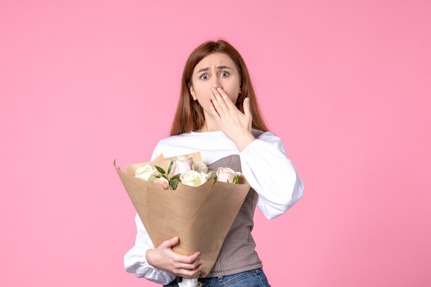 Junge Frau der Vorderansicht, die Blumenstrauß von schönen Rosen auf Rosa hält