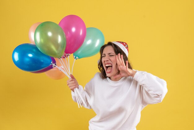 Junge Frau der Vorderansicht, die bunte Luftballons hält, die auf Gelb schreien