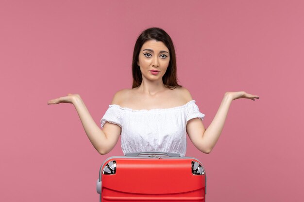 Junge Frau der Vorderansicht, die für Urlaub mit ihrer roten Tasche auf der rosa Hintergrundreise vorbereitet, die ins Ausland Seereise reist