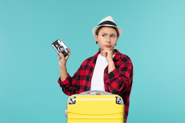 Junge Frau der Vorderansicht, die für Urlaub vorbereitet und Kamera auf blauem Schreibtisch hält