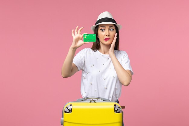 Junge Frau der Vorderansicht, die grüne Bankkarte auf rosa Schreibtischgefühlsommerfrauenreise hält