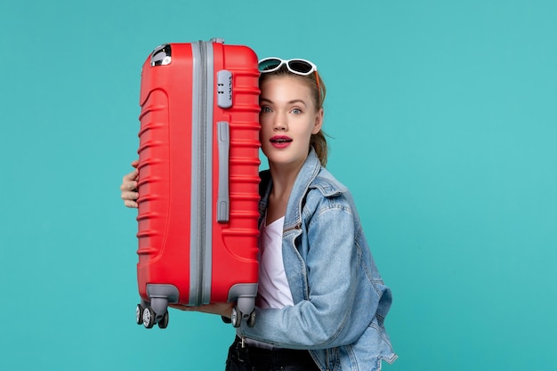Junge Frau der Vorderansicht, die ihre rote Tasche hält und sich auf die Reise auf der Reise der blauen Bodenreise-Urlaubsreise Meer vorbereitet