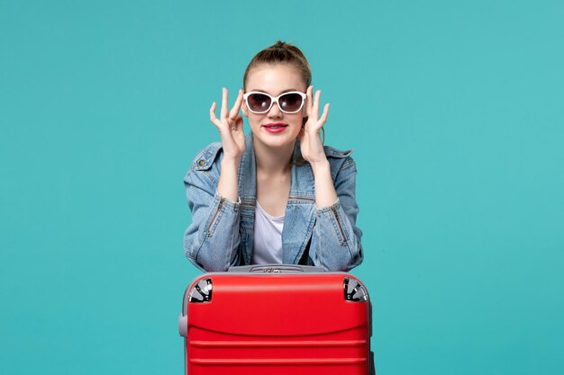 Junge Frau der Vorderansicht, die ihre Sonnenbrille trägt und sich auf Urlaub auf blauem Raum vorbereitet