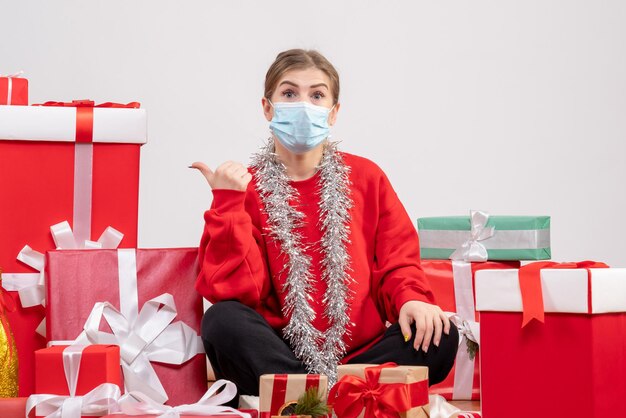 Junge Frau der Vorderansicht, die mit Weihnachtsgeschenken in der sterilen Maske sitzt