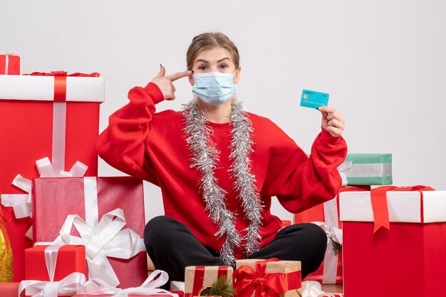 Junge Frau der Vorderansicht, die mit Weihnachtsgeschenken in der sterilen Maske sitzt