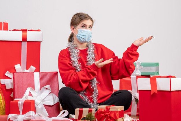 Junge Frau der Vorderansicht, die mit Weihnachtsgeschenken in der sterilen Maske sitzt