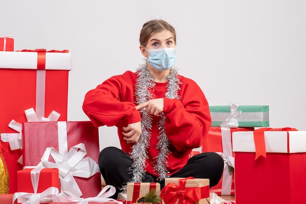 Junge Frau der Vorderansicht, die mit Weihnachtsgeschenken in der sterilen Maske sitzt