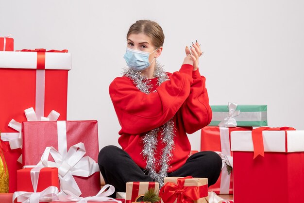 Junge Frau der Vorderansicht, die mit Weihnachtsgeschenken in der sterilen Maske sitzt