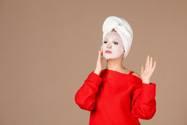 junge Frau der Vorderansicht, die vorbereitet, Gesichtsmaske auf rosa Hintergrund anzuwenden