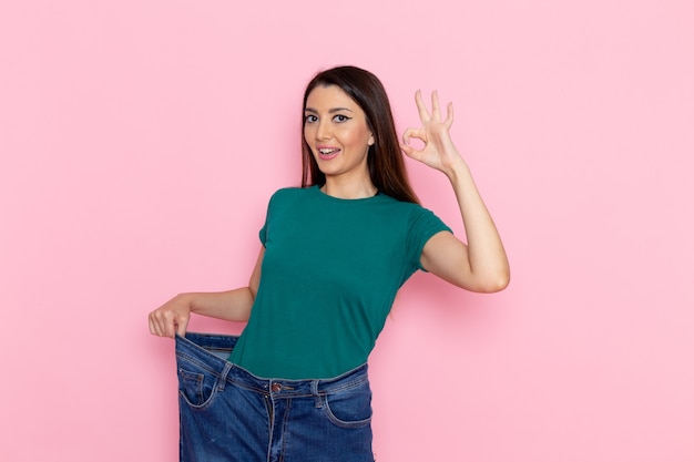 Junge Frau der Vorderansicht im grünen T-Shirt, das ihren schlanken Körper auf der rosa Wandtaille Sportübung Workout Beauty Slim Athlet zeigt