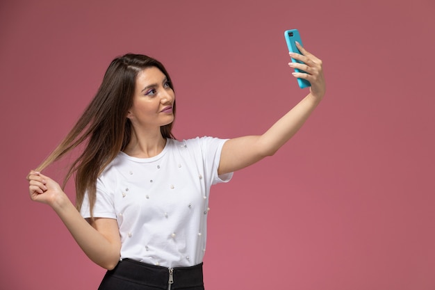 Junge Frau der Vorderansicht im weißen Hemd, das ein Selfie auf der rosa Wand, Modellfrauenhaltung nimmt