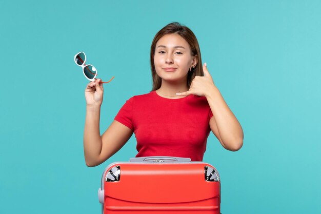 Junge Frau der Vorderansicht mit roter Tasche, die ihre Sonnenbrille auf dem blauen Raum hält