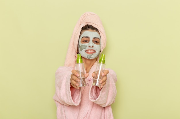 Junge Frau der Vorderansicht nach der Dusche im rosa Bademantel, der Make-up-Entferner auf grüner Oberfläche hält