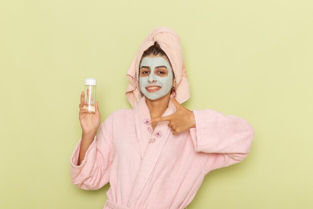 Junge Frau der Vorderansicht nach der Dusche im rosa Bademantel, der Spray auf einer grünen Oberfläche hält