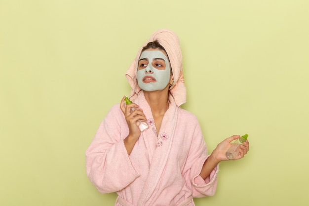 Junge Frau der Vorderansicht nach der Dusche im rosa Bademantel, der Sprays auf grünem Schreibtisch hält