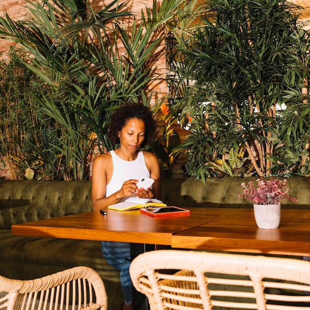 Junge Frau des Afroamerikaners, der intelligentes Telefon im Luxusrestaurant verwendet
