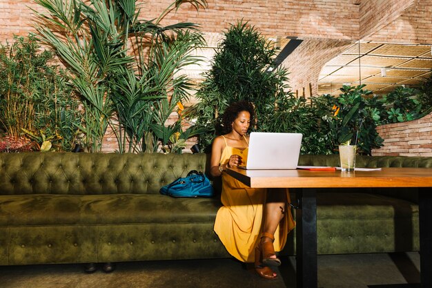 Junge Frau des Afroamerikaners, die im Restaurant unter Verwendung des Laptops sitzt