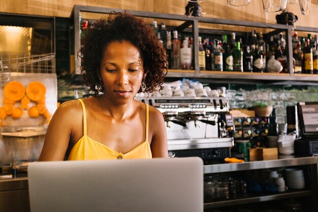 Junge Frau des Afroamerikaners, die Laptop am caf� verwendet