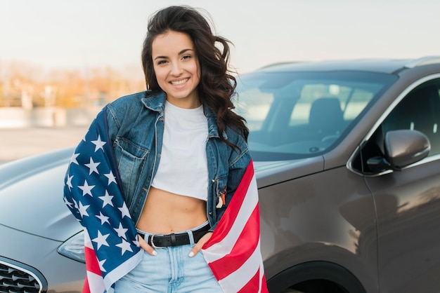 Junge Frau des mittleren Schusses, die große USA-Flagge nahe Auto trägt