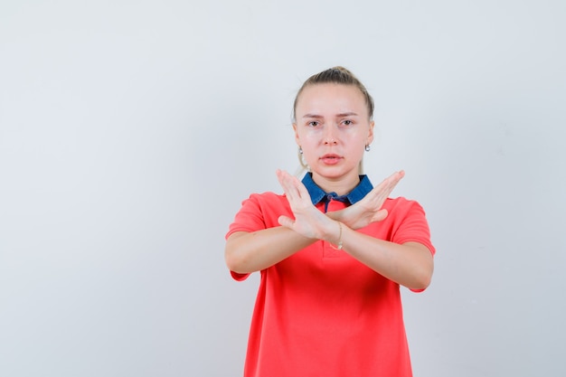 Junge Frau, die Ablehnungsgeste im T-Shirt zeigt und ernst schaut