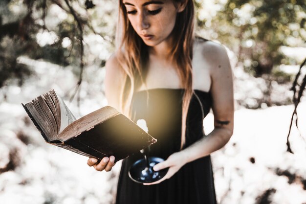 Junge Frau, die altes Buch mit Kerze im Holz liest