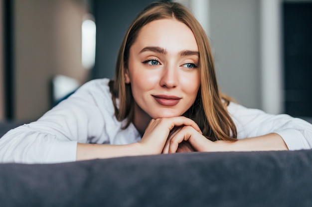 Junge Frau, die am Ende des Bettes unter der Steppdecke liegt und lächelt, den Kopf auf die Hand gestützt, den anderen im Haar in