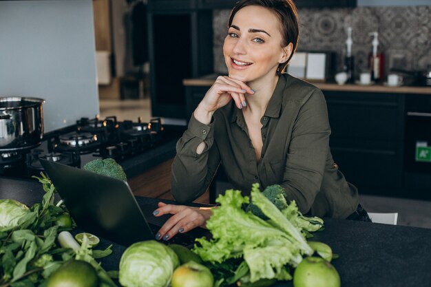 Junge Frau, die am Laptop arbeitet und an der Küche sitzt