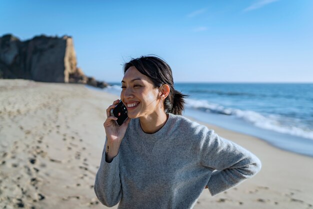 Junge Frau, die am Strand mit dem Smartphone spricht