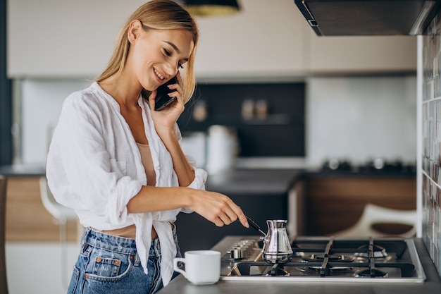 Junge Frau, die am Telefon spricht und Morgenkaffee kocht