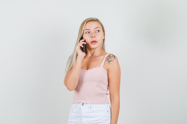 Junge Frau, die am Telefon spricht, während sie im Unterhemd beiseite schaut