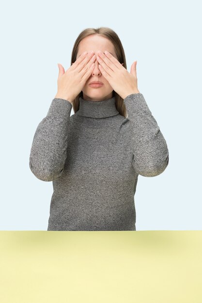 Junge Frau, die am Tisch im Studio mit geschlossenen Augen lokalisiert auf Blau sitzt. Ich kann nichts sehen