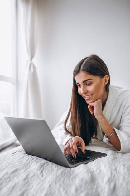 Junge Frau, die an Computer im Bett arbeitet