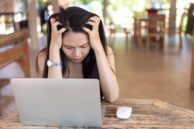 Junge Frau, die an dem Laptop hat Kopfschmerzen arbeitet.