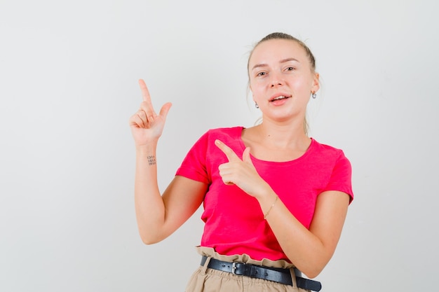 Junge Frau, die an der oberen linken Ecke in den rosa T-Shirts und in der Hose zeigt und fröhlich aussieht