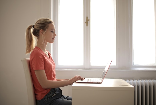 Junge Frau, die an ihrem Laptop auf einem Tisch in einem Raum arbeitet