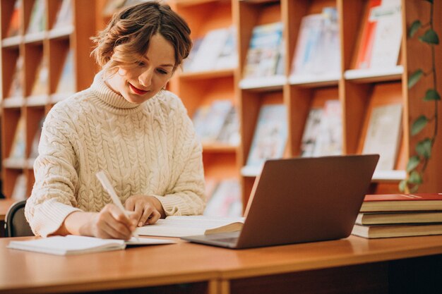 Junge Frau, die an Laptop in einer Bibliothek arbeitet