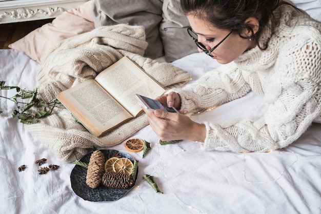 Junge Frau, die auf Bedsheet mit Handy liegt